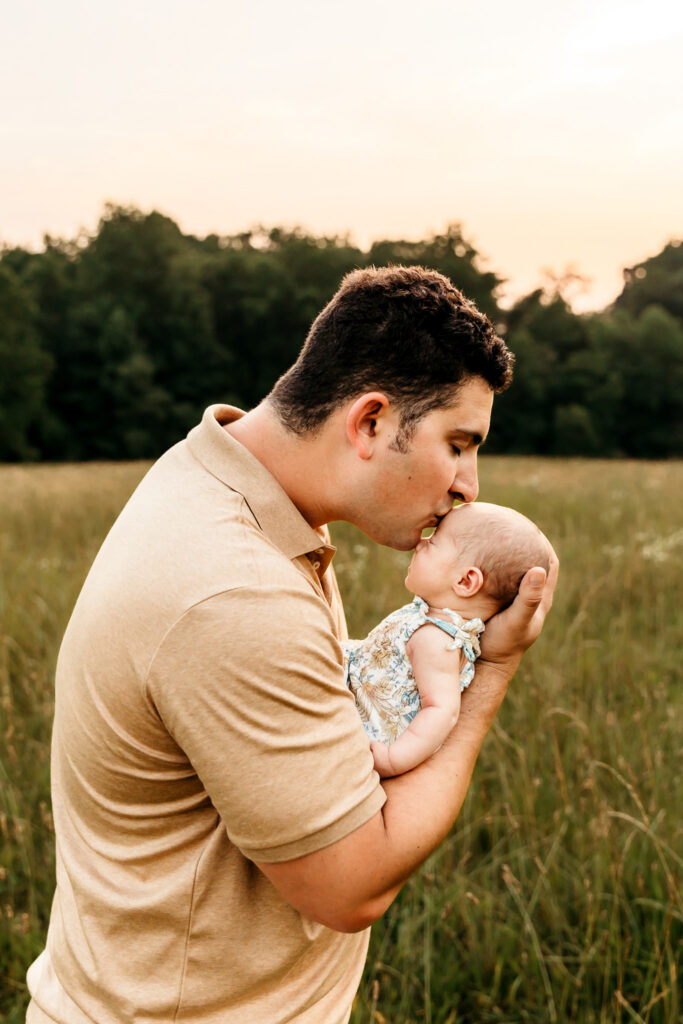 Dad kissing his baby daughter's head in a golden field