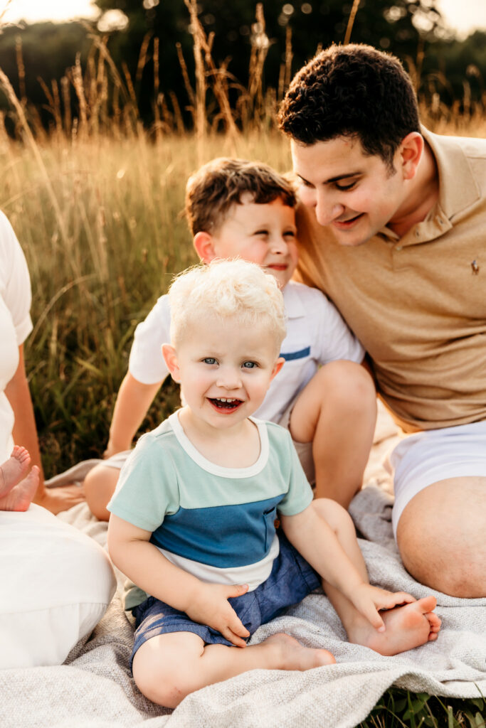 Dad snuggling his two young sons on a blanket during a golden summer evening in Statesville