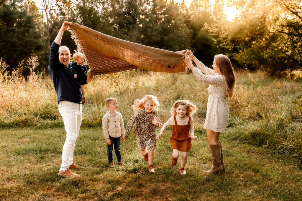 Parents lifting a blanket over their kids, all dressed in earth tones, as they run through a field
